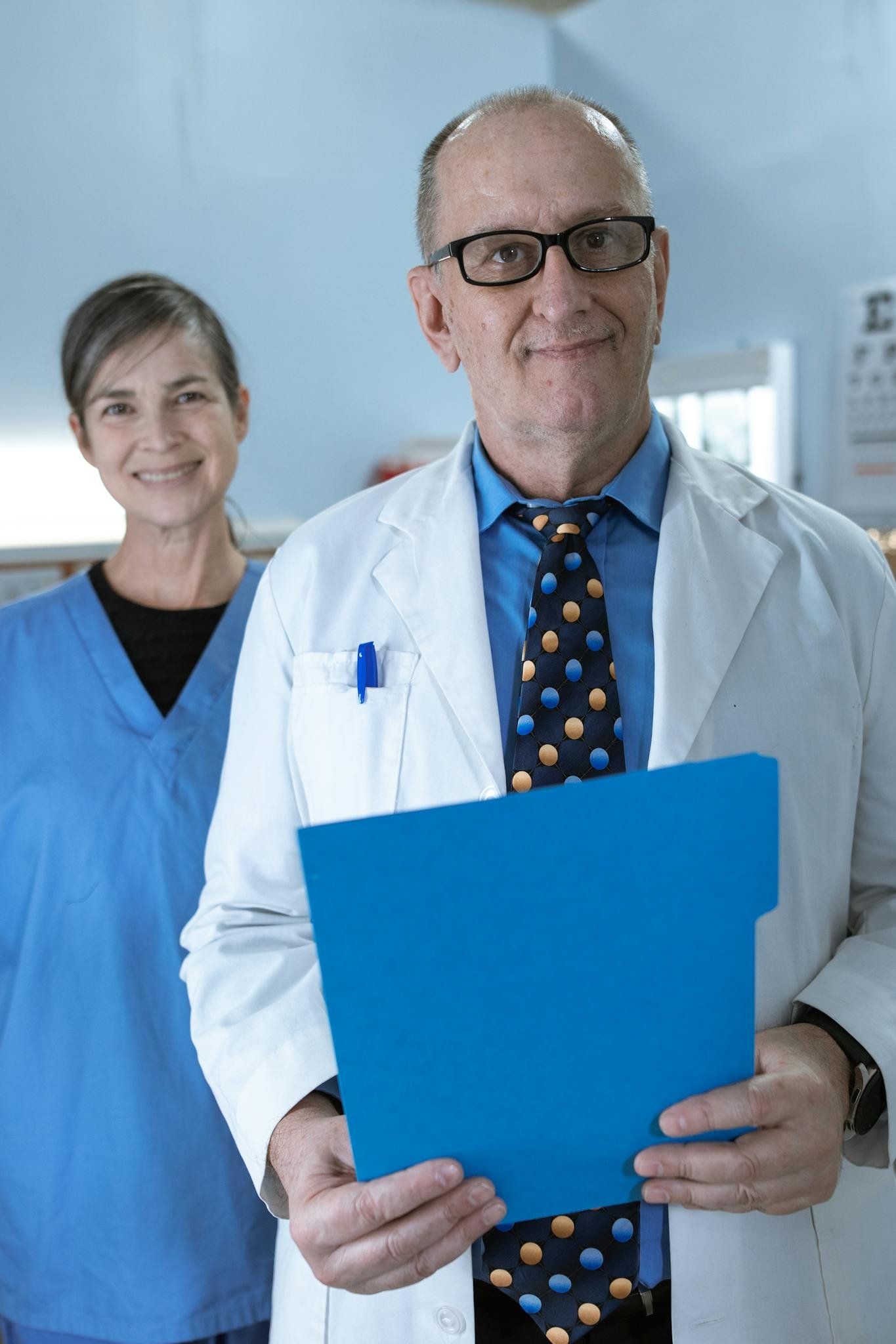 Smiling doctors in scrubs and lab coat holding medical file in a hospital.
