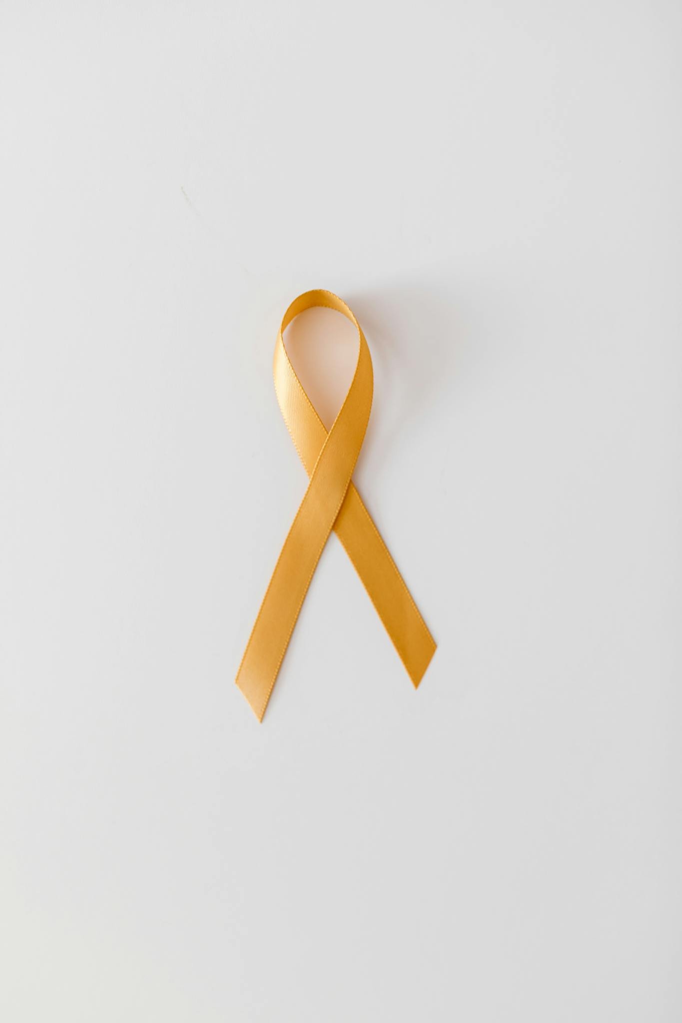 Yellow ribbon symbolizing cancer awareness on a minimalist white background.